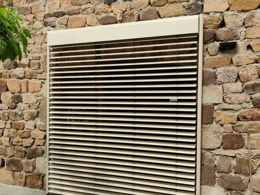 Brise-soleil orientable beige posé sur un mur en pierre