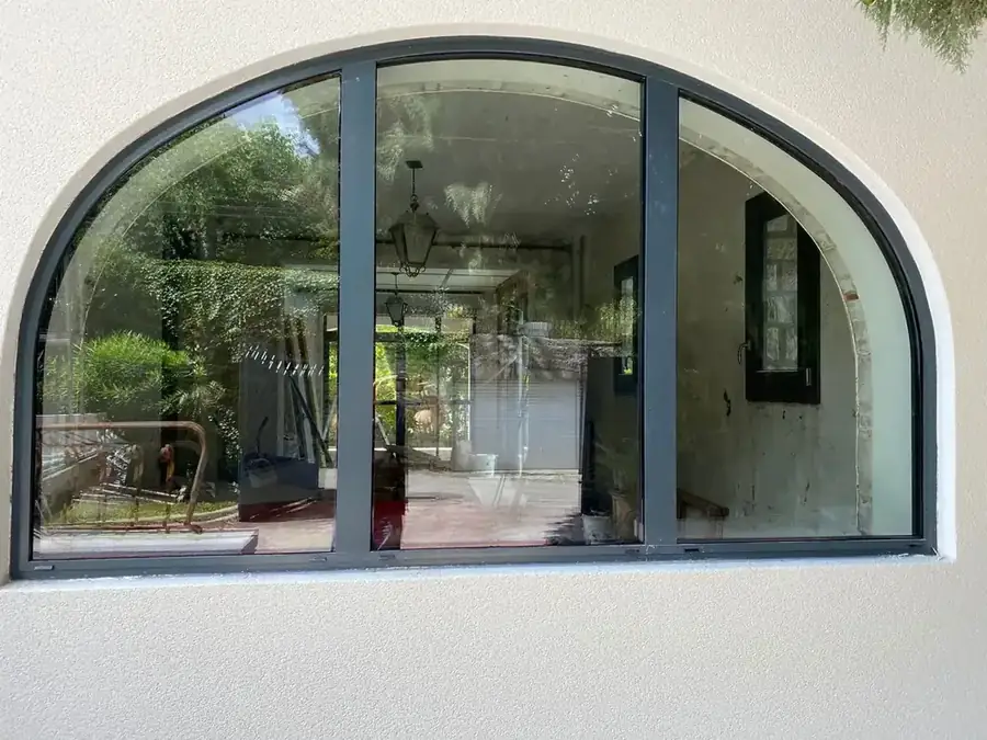 Fenêtre cintrée en aluminium gris foncé dans un mur crépi