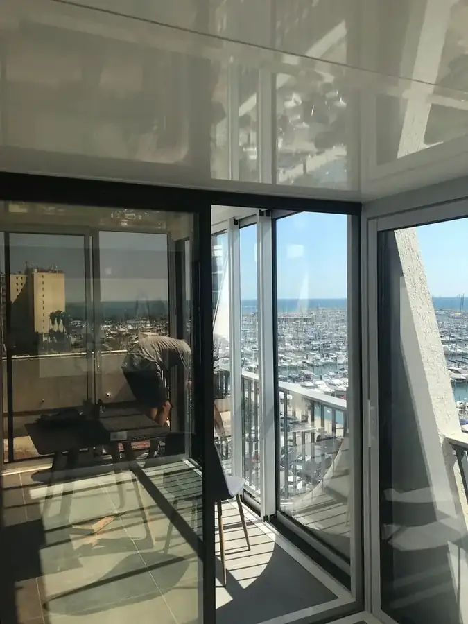Fermeture de balcon vitrée en cours de pose, vue sur un port de plaisance