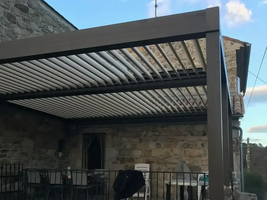 Pergola bioclimatique anthracite aux lames ouvertes, adossée à une maison en pierre