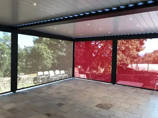Pergola bioclimatique à lames avec stores verticaux en toile rouge, sol dallé en pierre