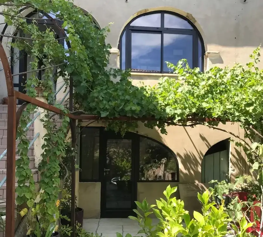 Porte vitrée et fenêtre cintrée en aluminium noir sous une treille de vigne