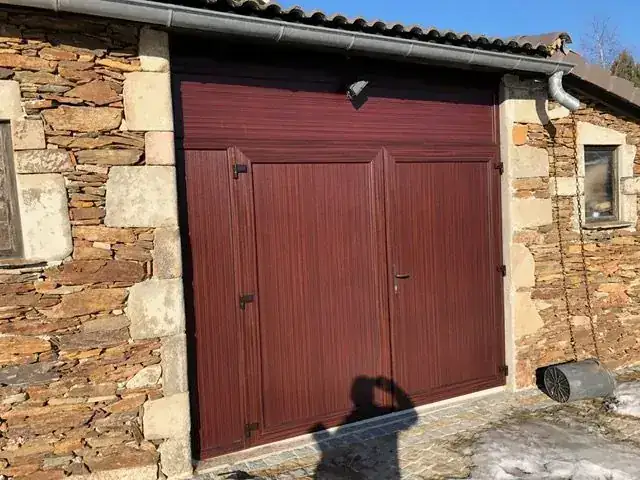 Porte de garage battante bordeaux sur un bâtiment en schiste