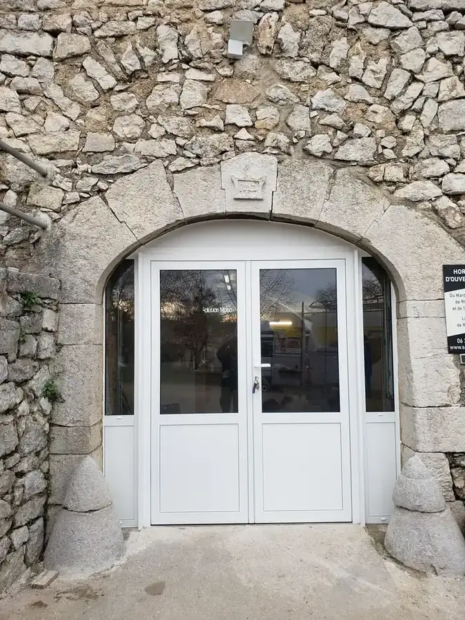 Porte vitrée PVC blanc à double vantail dans une arche en pierre