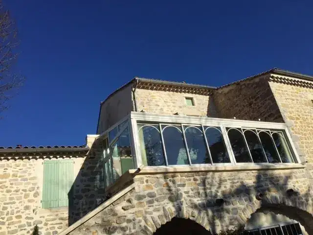 Véranda à arches vitrées accolée à une maison en pierre