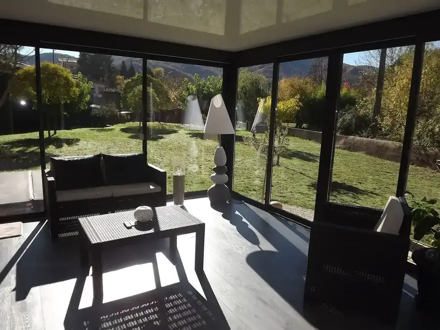Intérieur d'une véranda noire aménagée en salon, ouverte sur le jardin