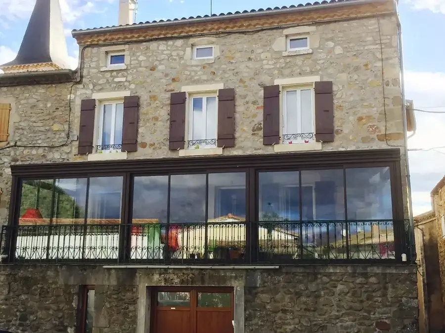 Fermeture vitrée en façade d'une maison de village en pierre aux volets bordeaux