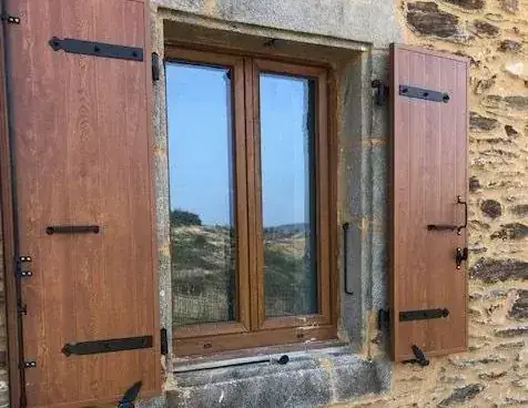 Fenêtre et volets battants ton bois aux pentures noires sur un mur en pierre