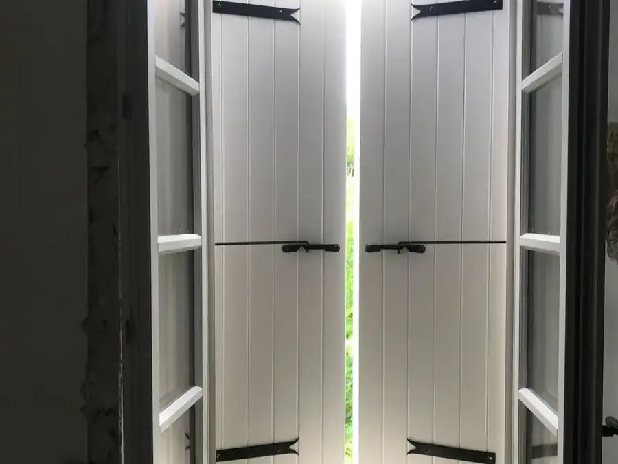 Volets intérieurs blancs entrouverts vus de l'intérieur